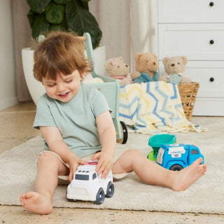 Child playing with toy cars on a rug in a room with teddy bears and a dresser.