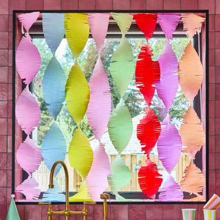 Colorful paper fan decorations on a window with a pink wall background