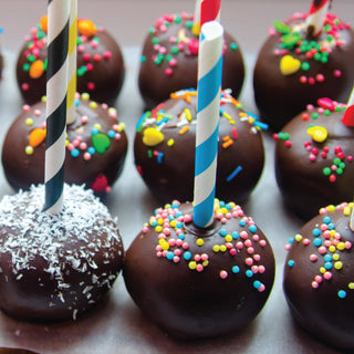 Chocolate-dipped treats with colorful sprinkles and straws on a white surface