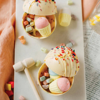 Decorative ice cream-shaped smash cake with colorful toppings on a marble surface.