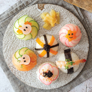 Plated sushi art with smiley face designs on a textured stone surface