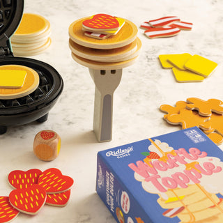 Maple Topples game set with toy waffle maker, wooden pieces, and box on a light surface.