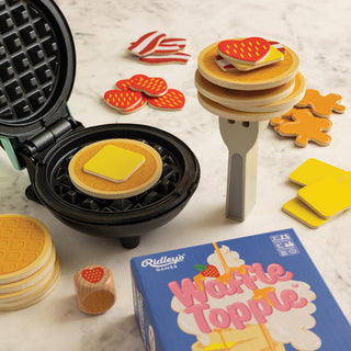Waffle Topple game set with waffle maker, wooden pieces, and game box on a marble surface