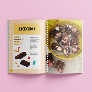 Open book showing a recipe for Rocky Road with a bowl of rocky road on a pink background