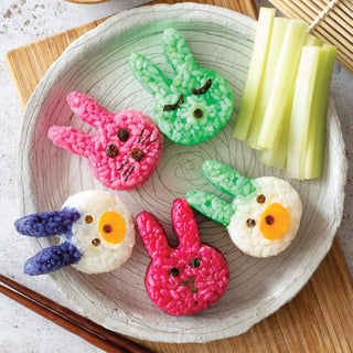 Colorful bunny-shaped rice cakes on a plate with sticks of celery.